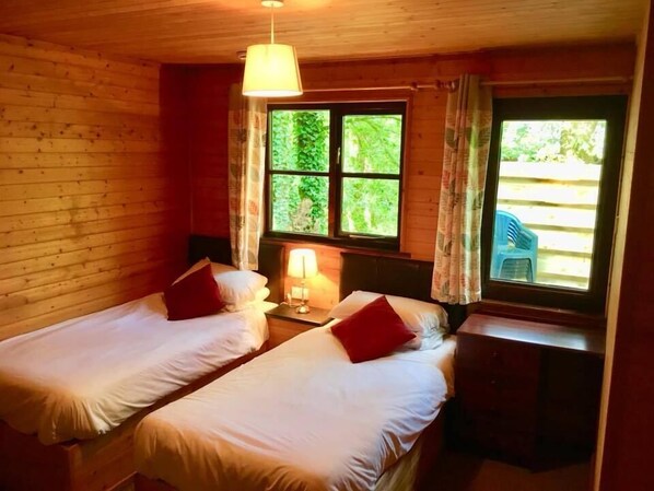 A room with two single beds, a nightstand with a lamp, and a window with curtains.