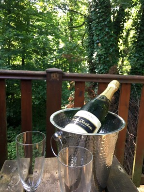 Un balde de metal con una botella de champán y dos copas sobre una mesa de madera al aire libre.
