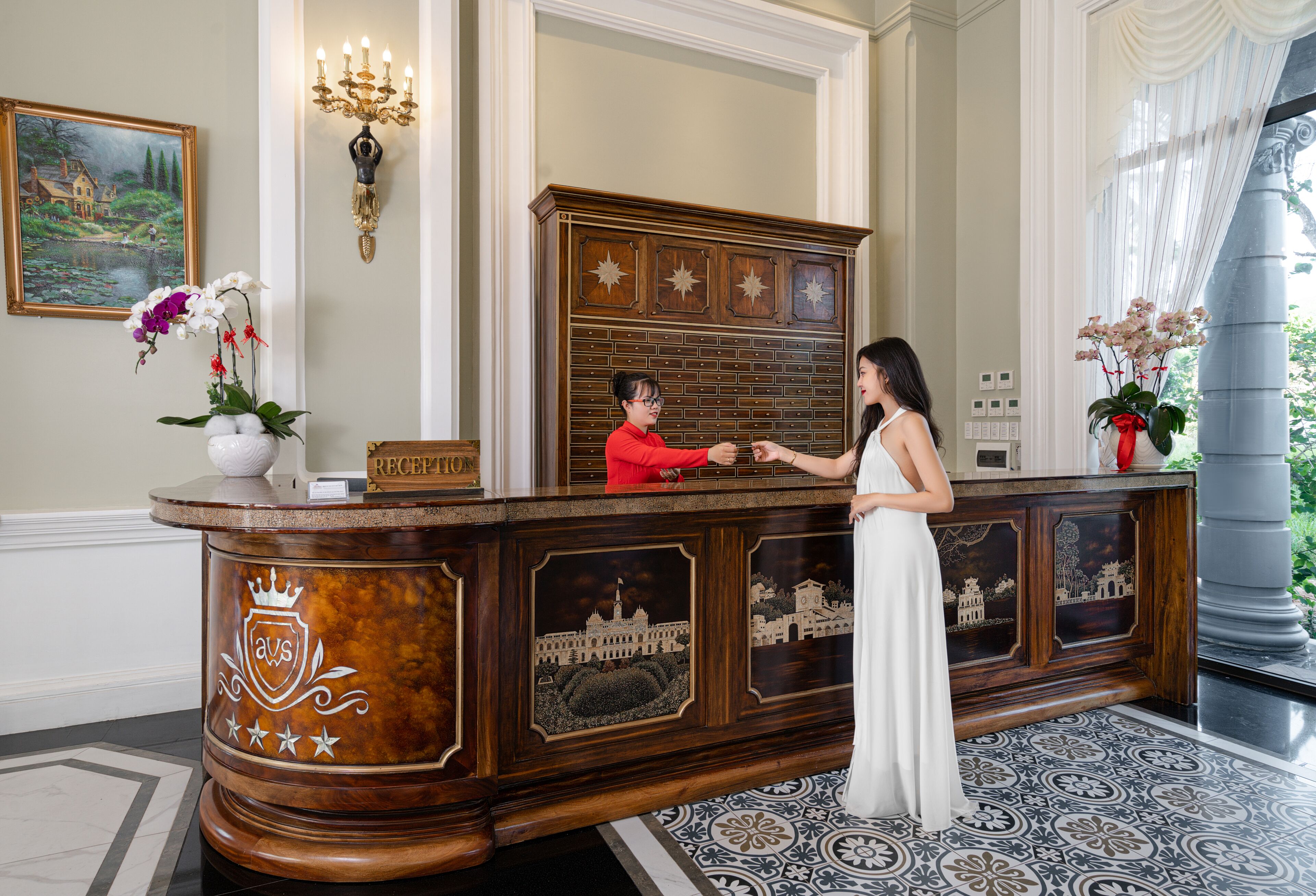 A reception desk with a coat of arms, a chandelier, and a painting on the wall.