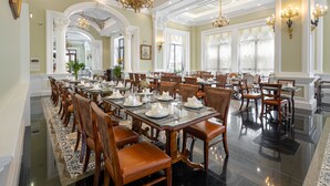 A formal dining room with multiple tables set for service, ornate chandeliers, and classical architecture.