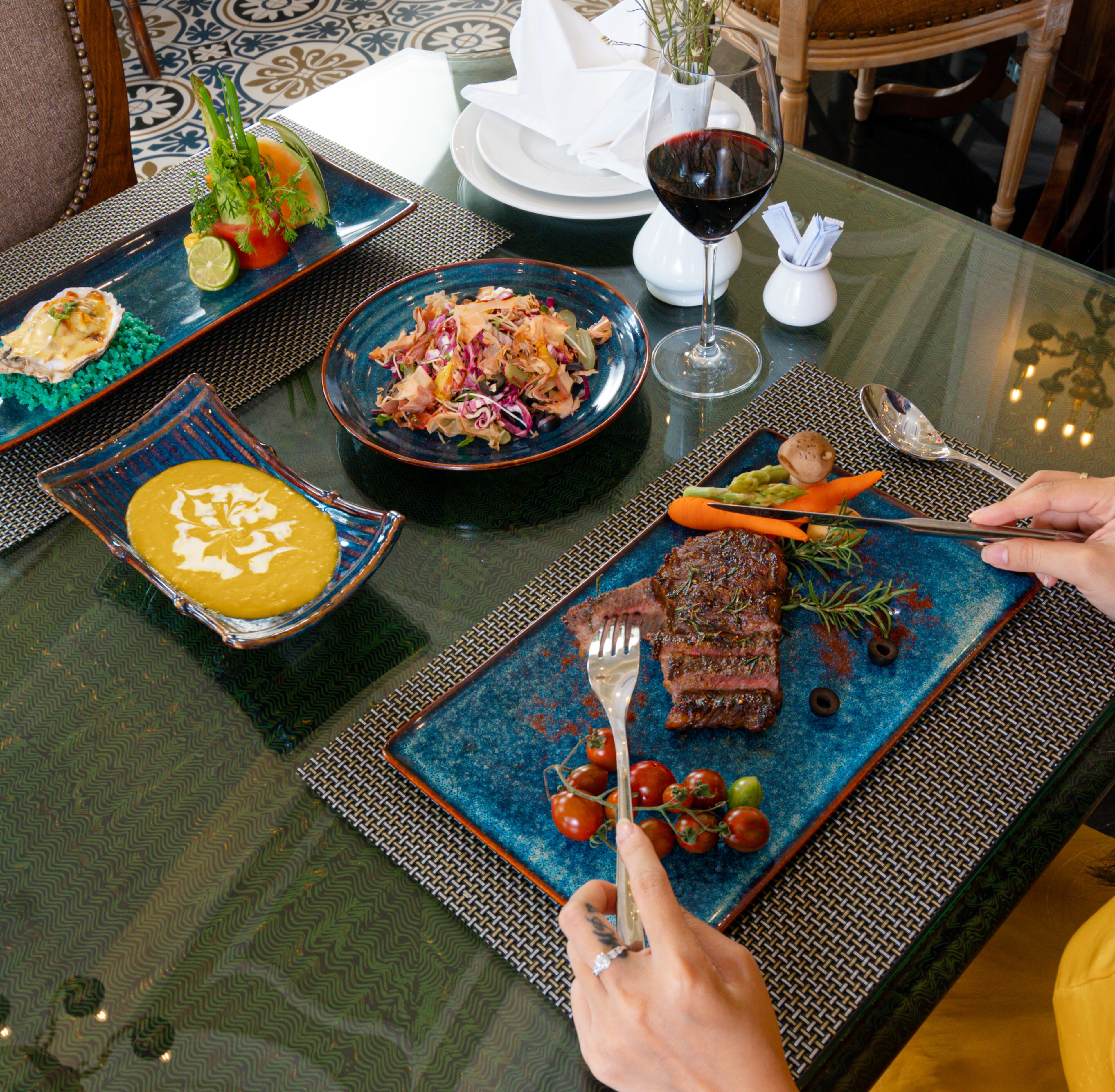 A dining table with various dishes, including a steak, salad, and soup.