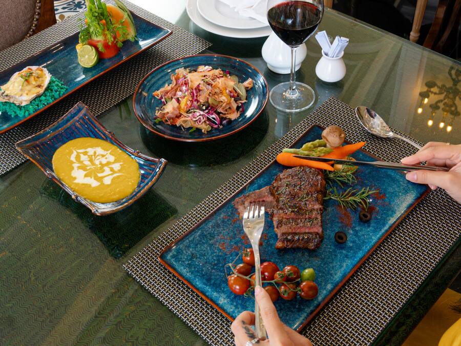 A dining table with various dishes, including a steak, salad, and soup.
