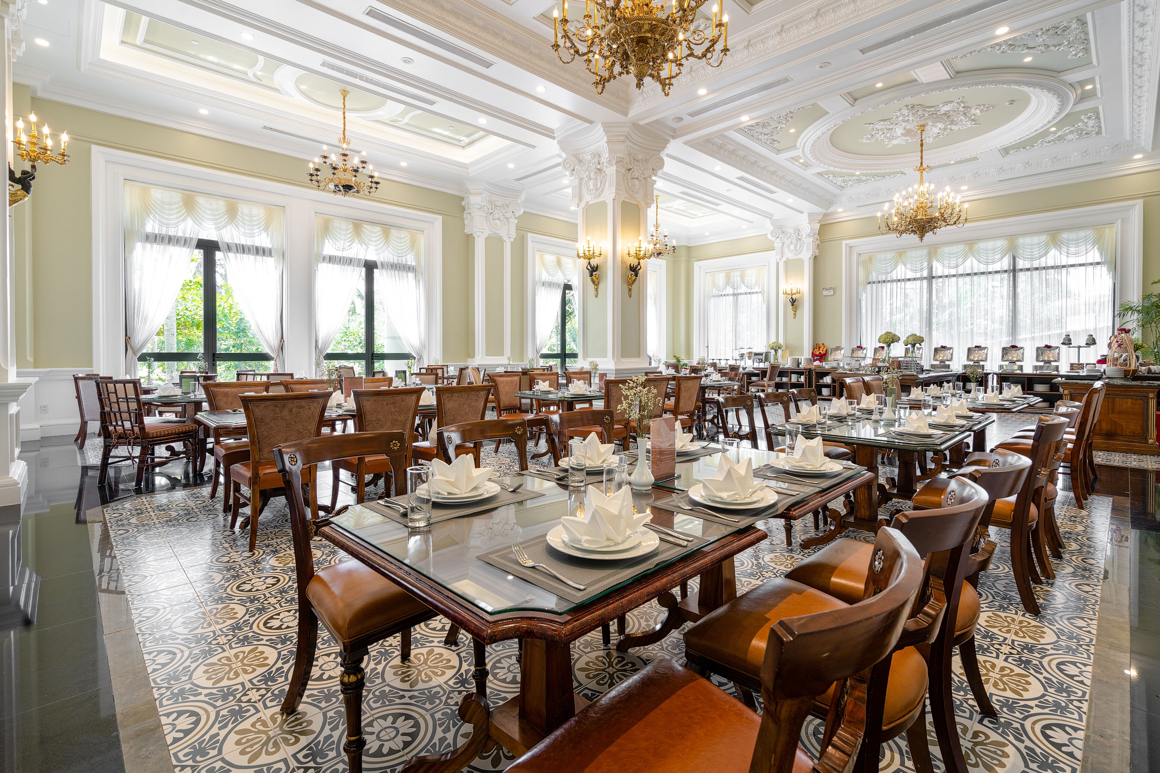 A spacious dining area with ornate chandeliers, large windows, and a polished floor.