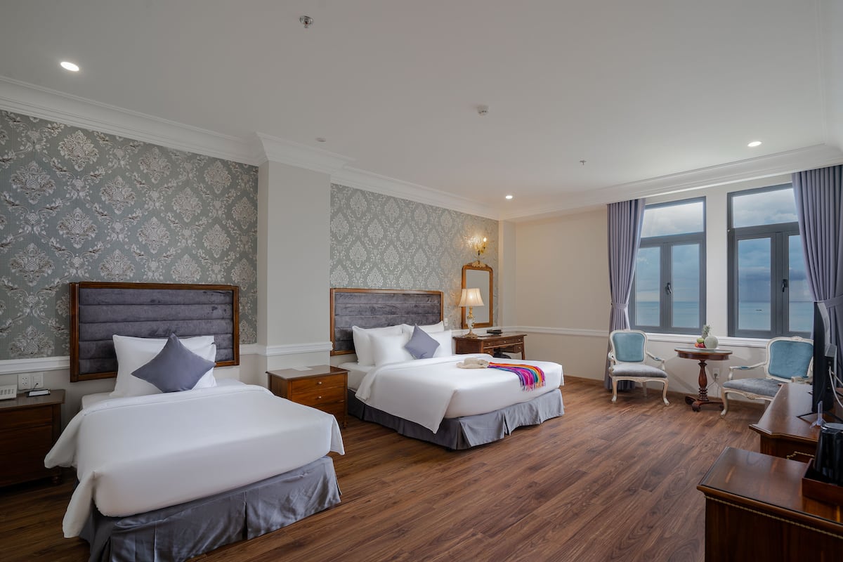 A hotel room with two beds, a desk, a chair, and a large window with curtains.