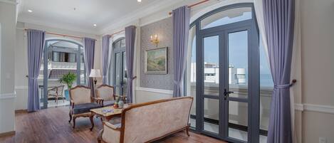 A spacious room with a wooden floor, a sofa, a dining table, and a view through a large glass door.