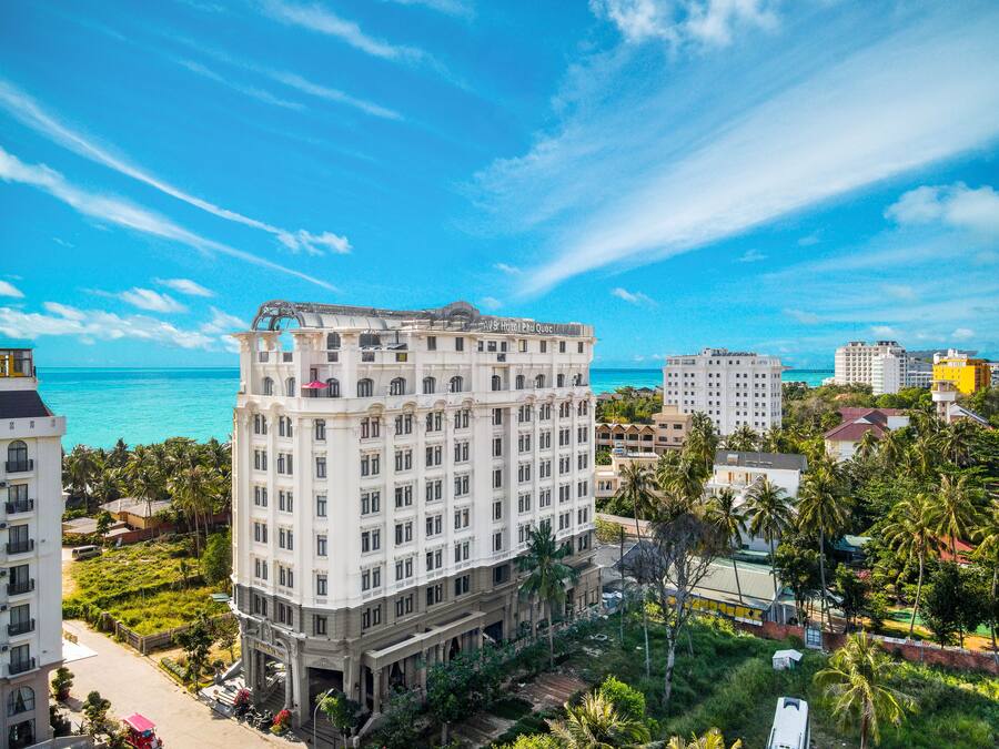 A multi-story hotel with a central courtyard, surrounded by lush greenery and a view of the ocean.