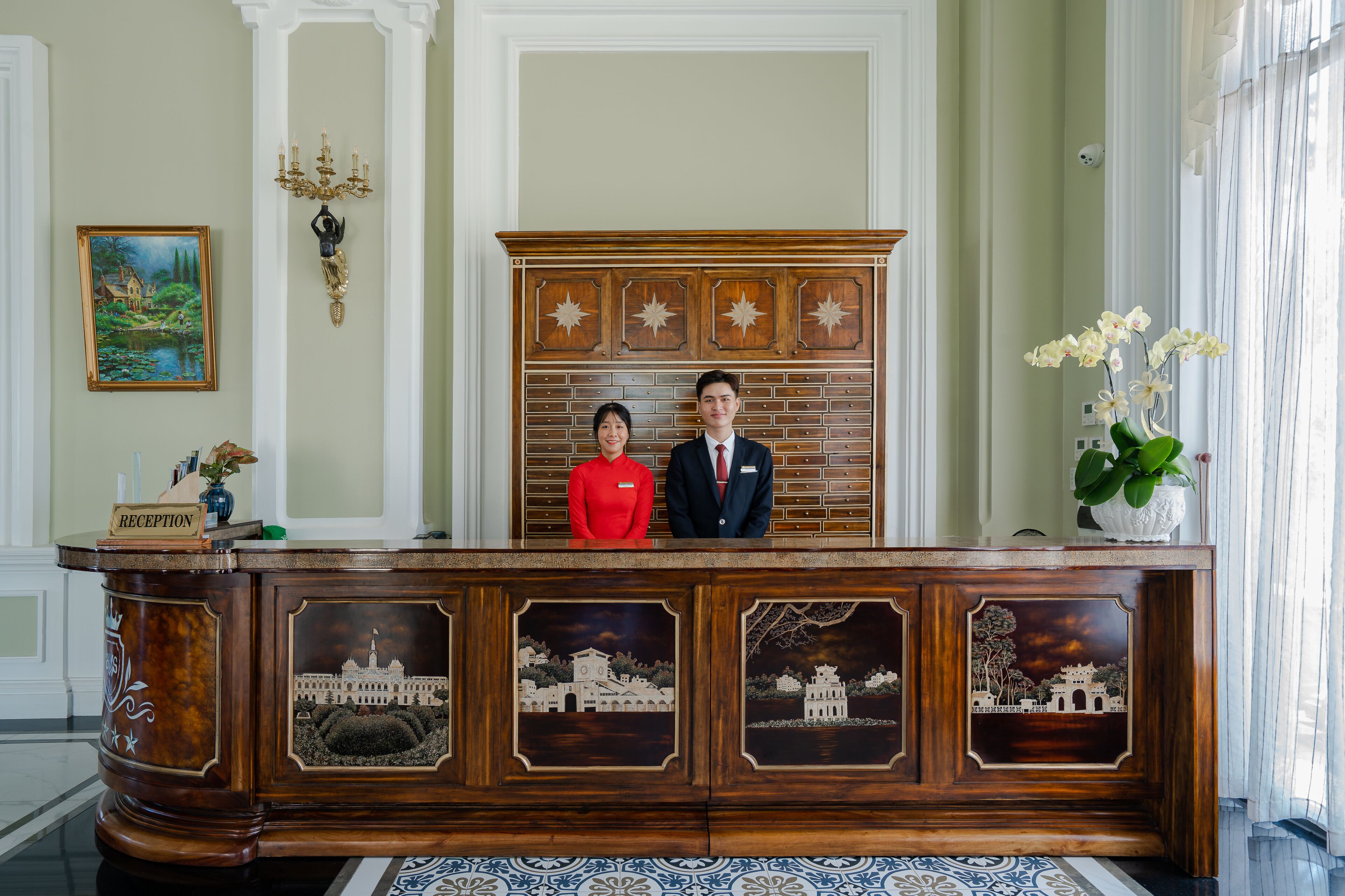 A reception desk with a wooden finish, a chandelier, and a painting on the wall.