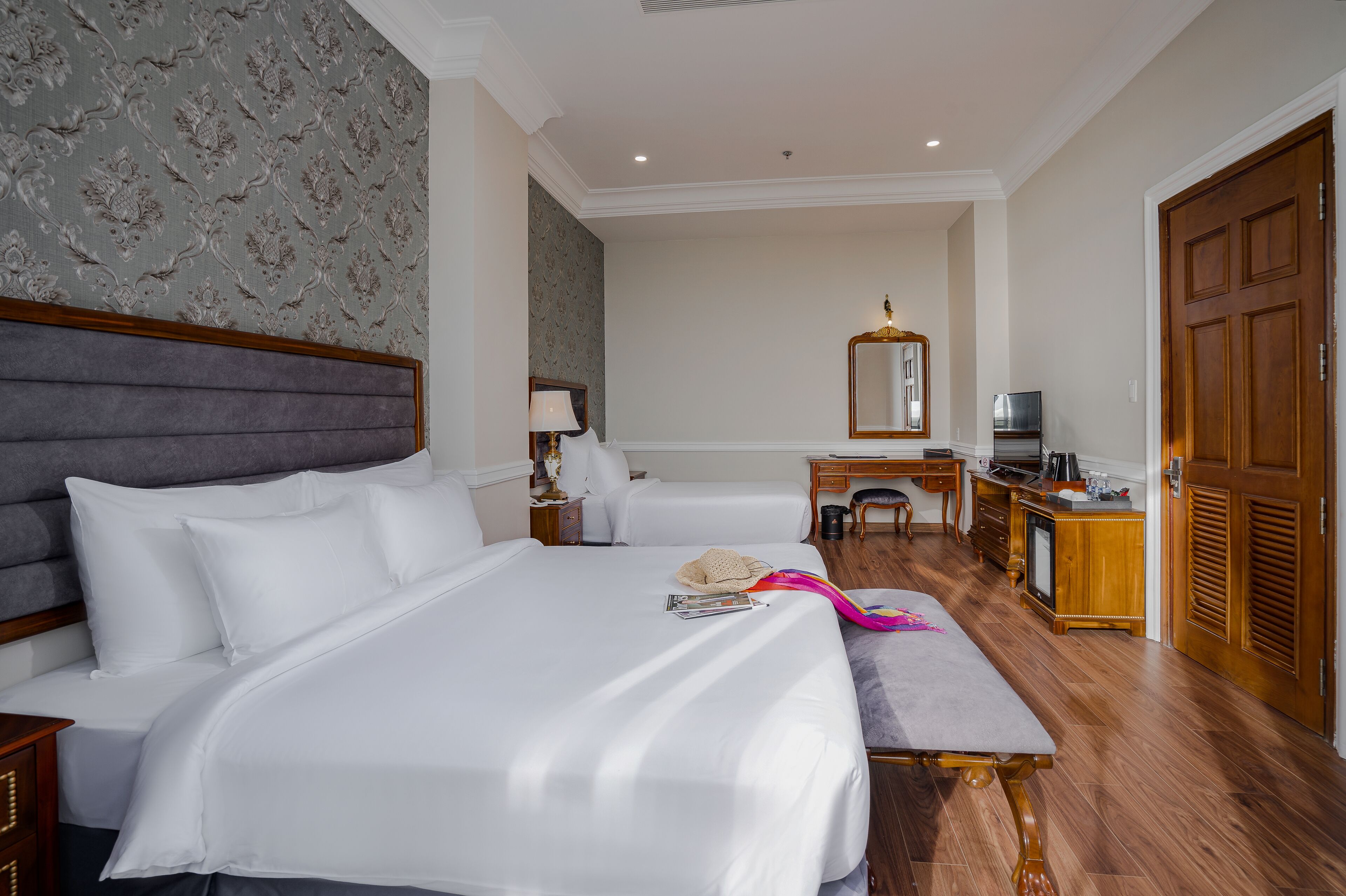 A hotel room with two beds, a desk, a chair, a television, and a wardrobe.