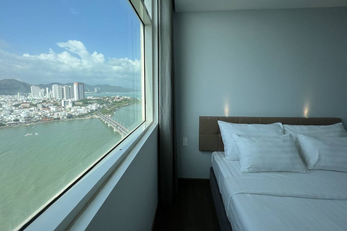 A hotel room with a large window offering a view of a cityscape and a bridge over water.