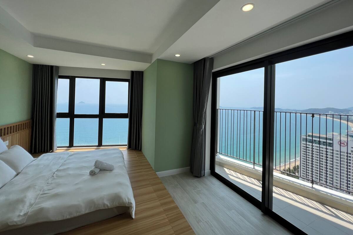 A hotel room with a large bed, a view of the sea, and a balcony with a railing.