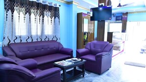 Una habitación con un sofá morado, una mesita con revistas y un televisor montado en la pared.