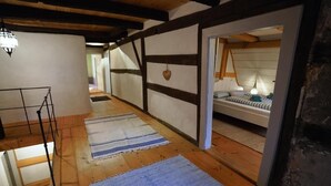 A narrow hallway with wooden floors, a staircase, and a bed with a striped bedspread in the background. - Rent one of the oldest houses in Weissenburg's old town for up to 9 people (Weißenburg in Bayern)