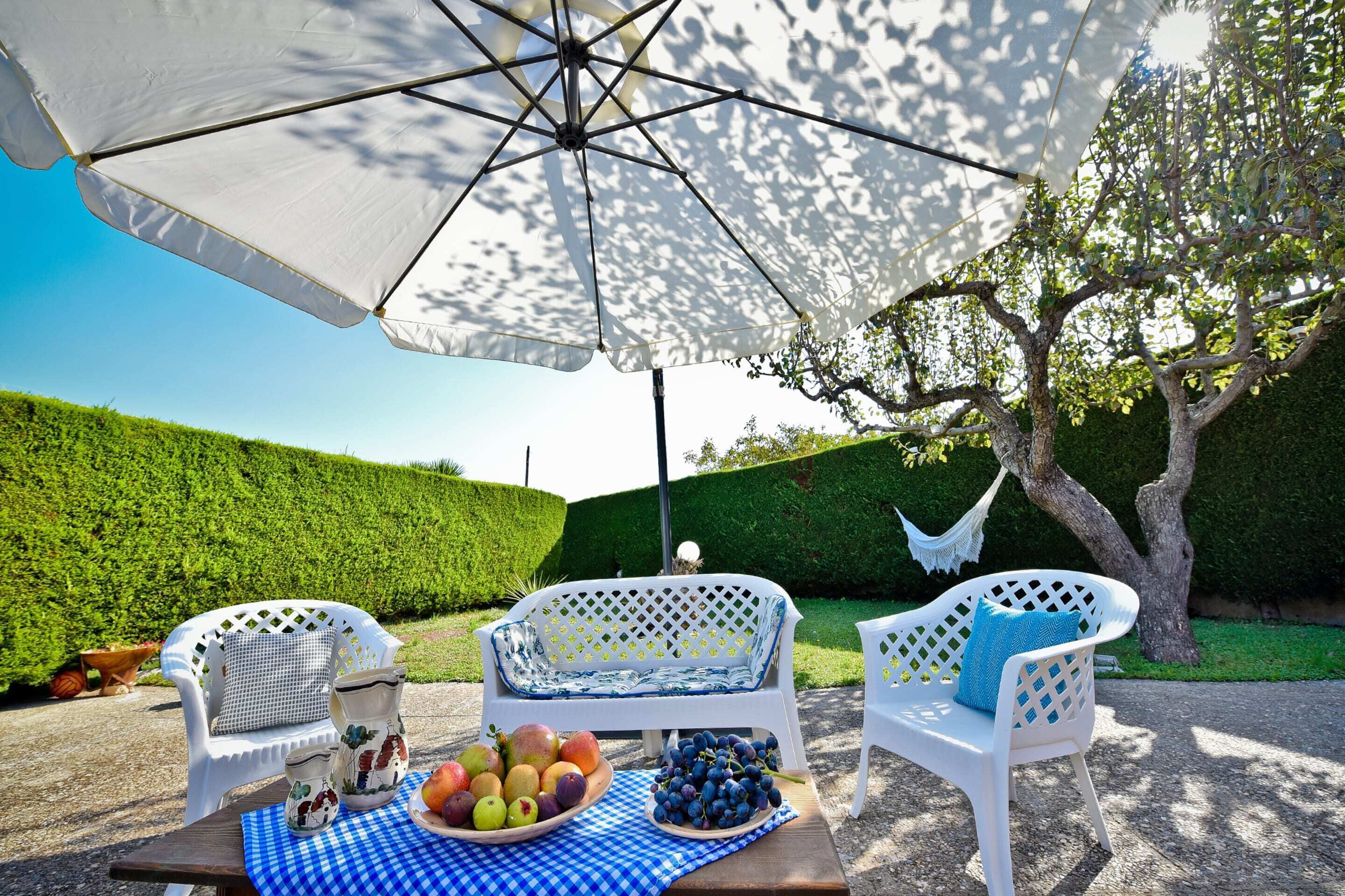 An outdoor seating area with white chairs, a table with a checkered tablecloth, and a large umbrella providing shade.