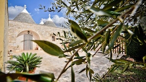 A courtyard with stone buildings, a potted plant, and a clear blue sky. - I Cinque Trulli with Swimming Pool (Martina Franca)