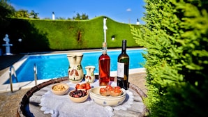 A poolside table with a bottle of red wine, a bottle of white wine, a bowl of olives, a bowl of chickpeas, and a plate of tomatoes. - I Cinque Trulli with Swimming Pool (Martina Franca)
