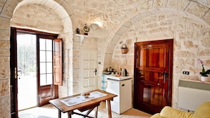 A stone-walled room with a wooden table, a small kitchenette, and a sofa. - I Cinque Trulli with Swimming Pool (Martina Franca)