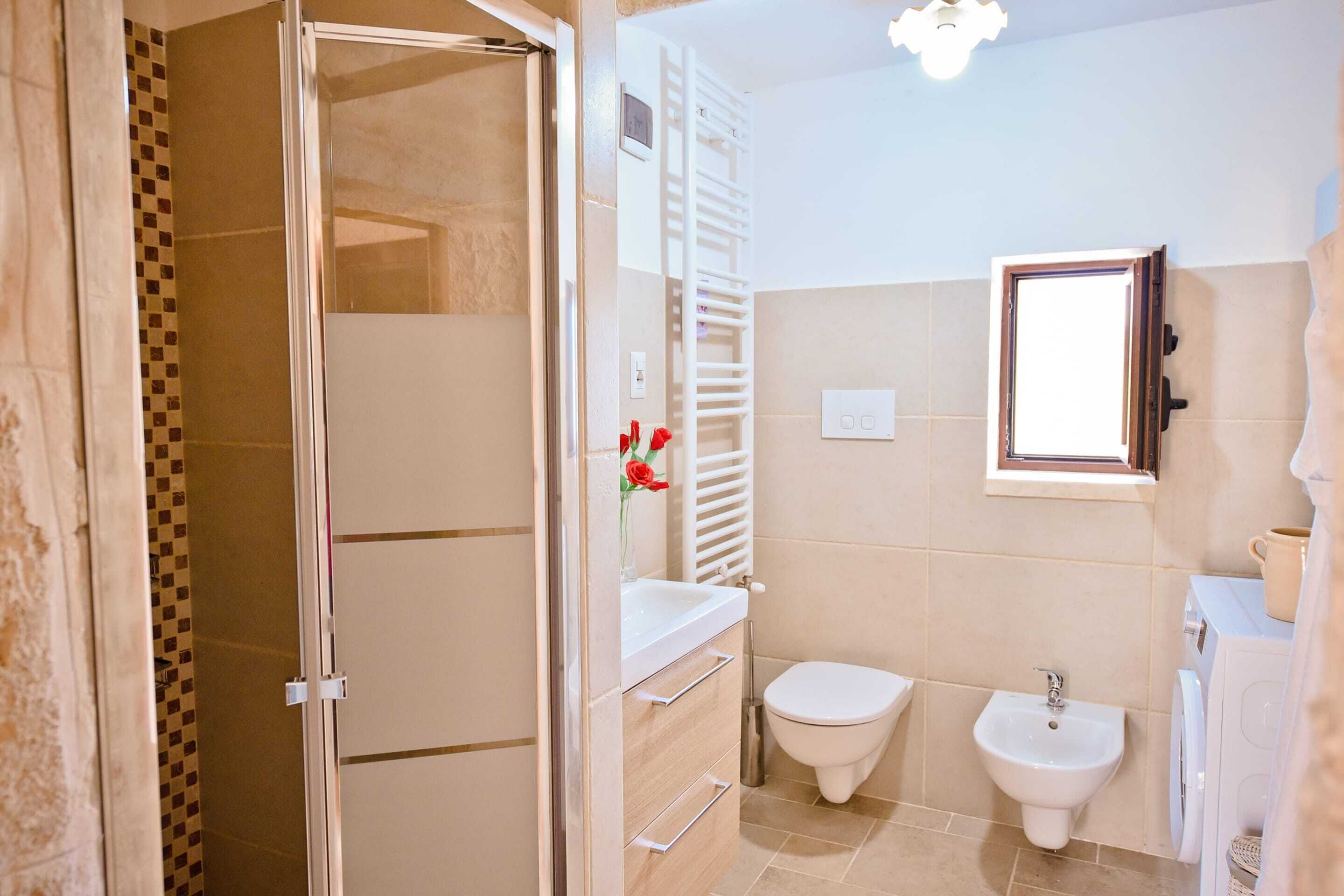 A bathroom with a shower, toilet, bidet, and a small window.