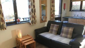 Ein Wohnzimmer mit einer Couch, einem kleinen Holztisch mit einer Lampe und Blick ins Freie durch große Fenster.