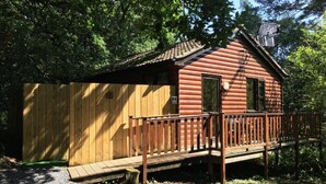 Eine Holzhütte mit Veranda und einer kleinen Terrasse, umgeben von Bäumen.
