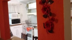 A kitchen with a red wall, a microwave, a stove, and a fruit bowl on the counter. - Suitable Season Rio das Ostras 021991484253 (Rio das Ostras)