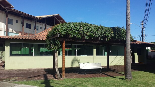 A building with a green facade, a tiled roof, and a bench under a pergola with climbing vines. - Suitable Season Rio das Ostras 021991484253 (Rio das Ostras)