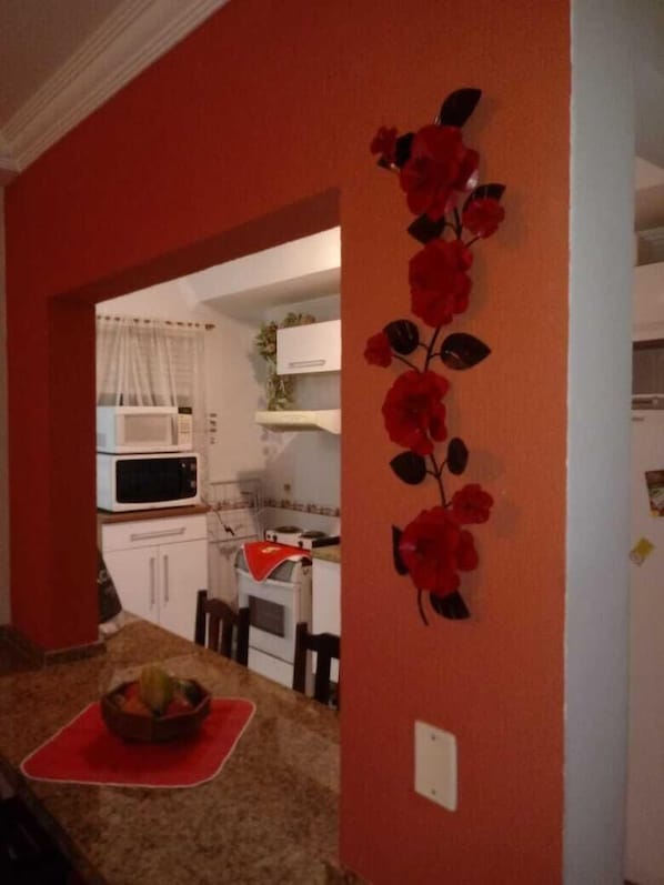 Une cuisine avec des meubles blancs, un four à micro-ondes et un élément décoratif rouge sur le mur.