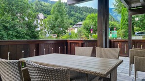 An outdoor seating area with wicker chairs and a table, overlooking a forested hillside. - Finest Villa Zell am See - Skihaserl (Zell am See)