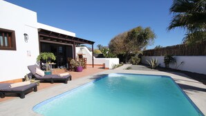 Une piscine rectangulaire avec des chaises longues et un patio couvert.