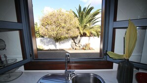 Une cuisine équipée d’un évier, d’une fenêtre et offrant une vue sur un arbre et un mur à l’extérieur.