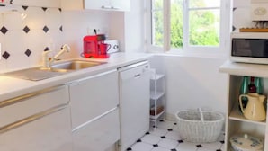 Una cocina con armarios blancos, una cafetera roja, un microondas y una ventana con vistas a zonas verdes.