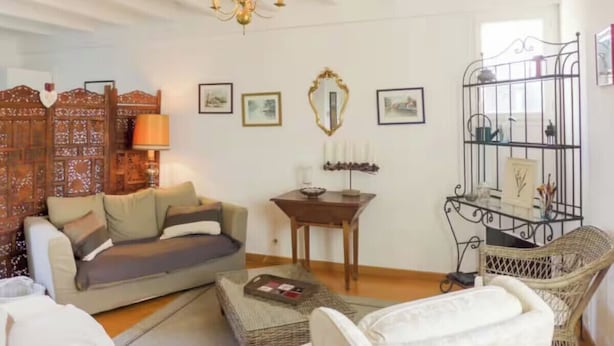 Una sala de estar con un sofá, una mesita, una silla, un espejo decorativo y una araña.