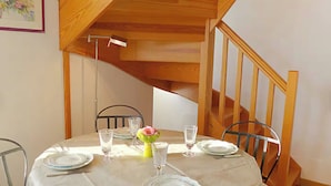 Una mesa de comedor dispuesta con platos, vasos y un florero con una flor, en una habitación con una escalera de madera.