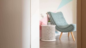 A modern room with a light blue armchair, a small white side table with a potted plant, and a geometric wall design. - Cosy 2-Bed Apartment in the Heart of Strathfield (Strathfield)