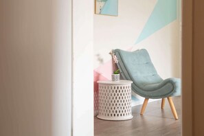 A modern room with a light blue armchair, a small white side table with a potted plant, and a geometric wall design. - Cosy 2-Bed Apartment in the Heart of Strathfield (Strathfield)