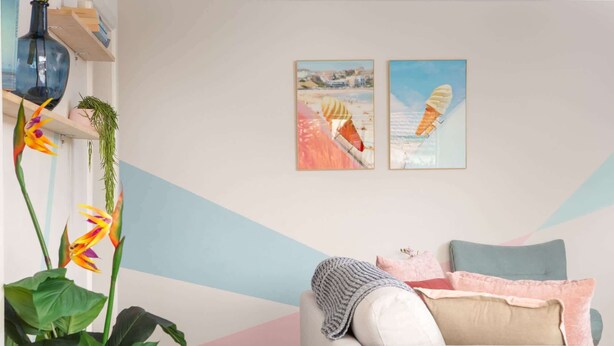 A living room with a sofa, cushions, a plant, and two beach-themed paintings on the wall. - Cosy 2-Bed Apartment in the Heart of Strathfield (Strathfield)