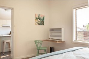 A bedroom with a bed, a green chair, a shelf unit, and a window with blinds. - Cosy 2-Bed Apartment in the Heart of Strathfield (Strathfield)