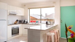 A modern kitchen with white cabinets, a built-in oven, a microwave, and a coffee maker. There is a window with a view of a building outside. - Cosy 2-Bed Apartment in the Heart of Strathfield (Strathfield)