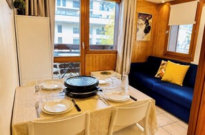 A dining area with a table set for two, a grill, and a blue sofa with a yellow pillow.