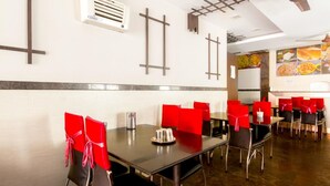 A restaurant with tables and chairs, a ceiling fan, and a wall-mounted air conditioner. - Rithikha Inn (Chennai)