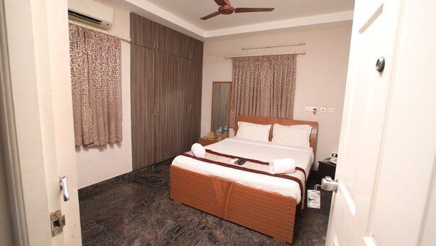 A hotel room with a bed, a wardrobe, a ceiling fan, and a bathroom door. - Rithikha Inn (Chennai)