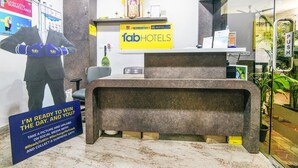A hotel reception area with a reception desk, a large poster of a man in a suit, and a sign for 'fabHOTELS'. - Rithikha Inn (Chennai)