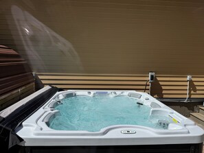 Ein Whirlpool mit Bedienfeld, umgeben von einer Holzterrasse und einer beigen Wand.