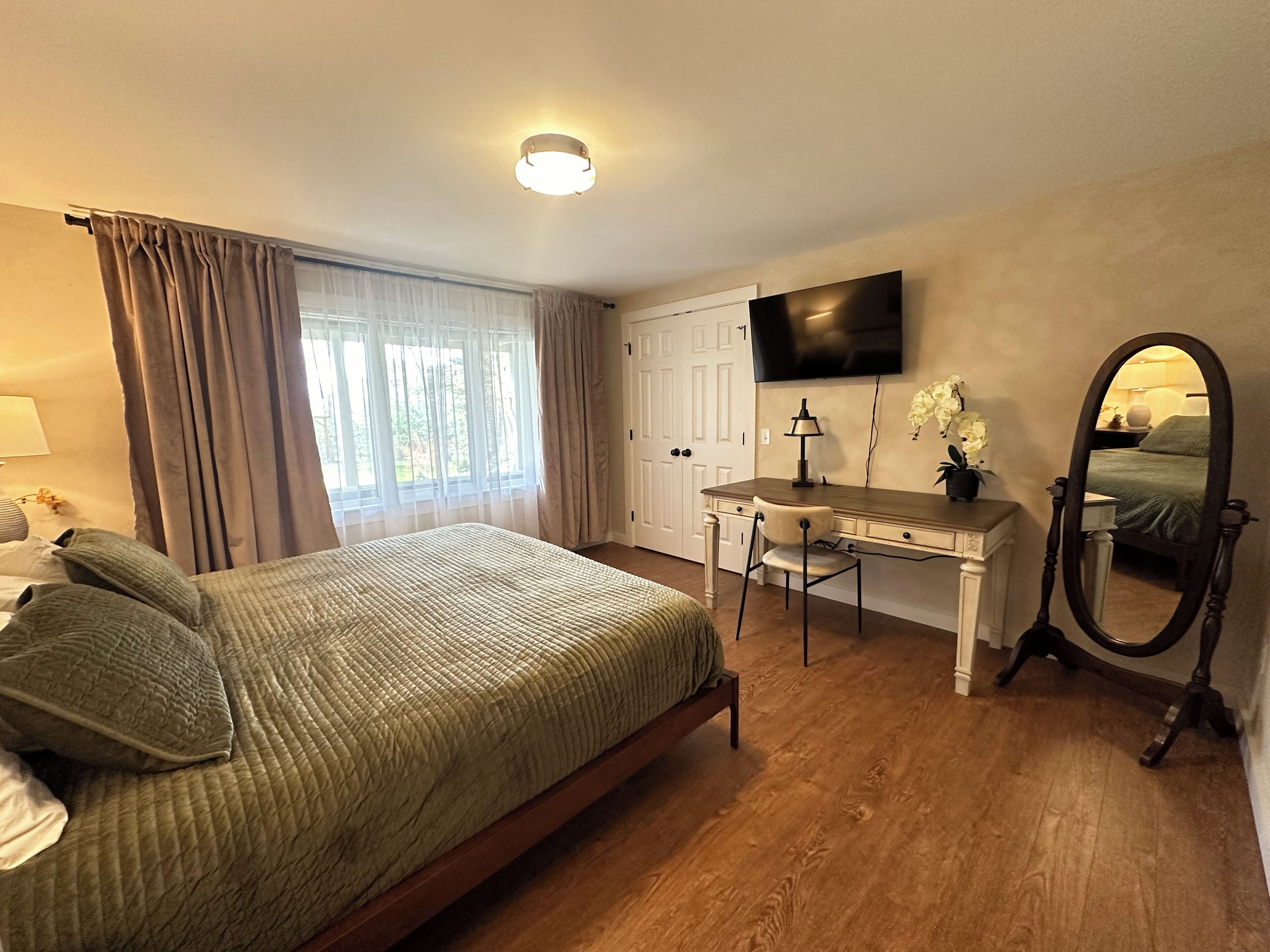 A bedroom with a bed, a desk, a chair, a TV, and a mirror.