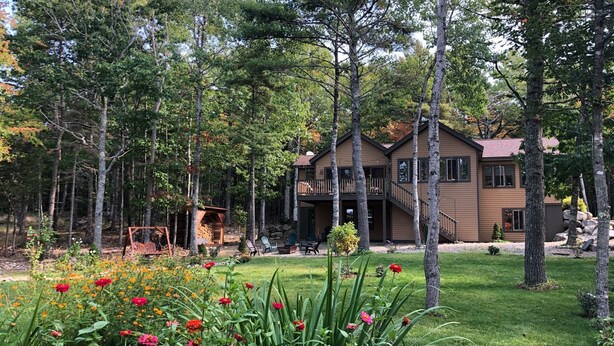 Ein zweistöckiges Haus, umgeben von einem Wald, mit einem gepflegten Rasen und Blumenbeeten.