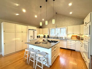 A modern kitchen with white cabinetry, a central island with stools, and pendant lighting.