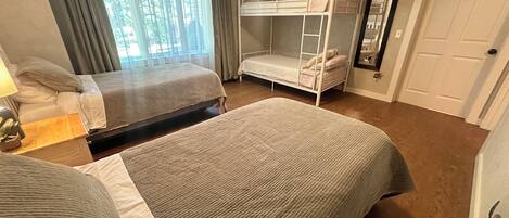A room with two bunk beds, a bedside table with a lamp, a window with curtains, and a door.