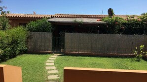 Een terras met betegelde vloer, een pad van stenen dat naar een poort leidt en een houten omheining.