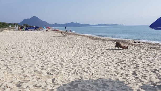 Een strand met een heldere lucht, een berg op de achtergrond en enkele mensen en parasols.