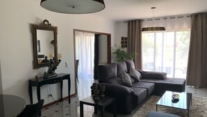 Ein modernes Wohnzimmer mit einer Couch, einem Couchtisch, einem Esstisch mit Stühlen und einem großen Fenster mit Vorhängen.