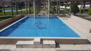 Ein rechteckiger Pool mit Kachelmuster, umgeben von einer Steindeck und einem überdachten Bereich mit Säulen.
